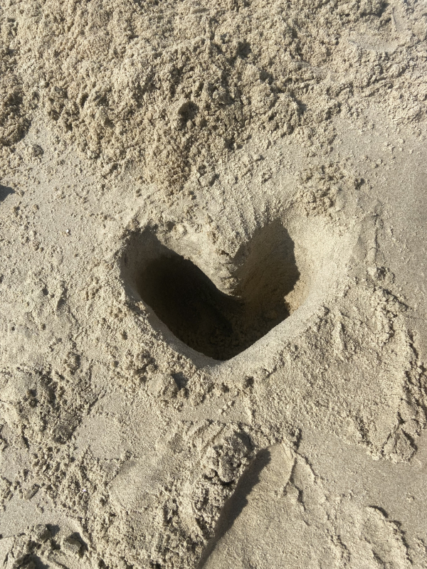 a hole dug into the beach sand in the shape of a heart